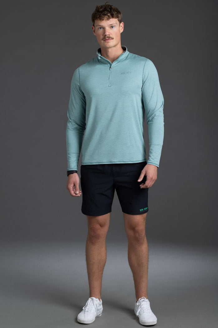 Man wearing a light blue long-sleeve shirt and black shorts on a gray background || Black