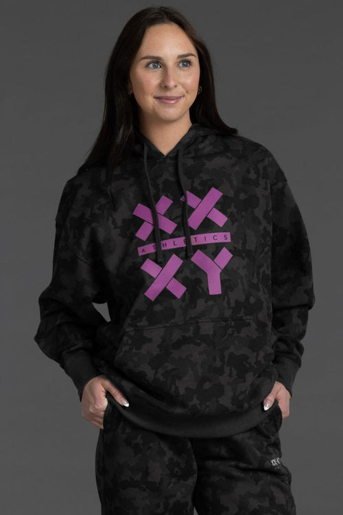 Person wearing a black camouflage hoodie with purple logo on a gray background || Black Camo