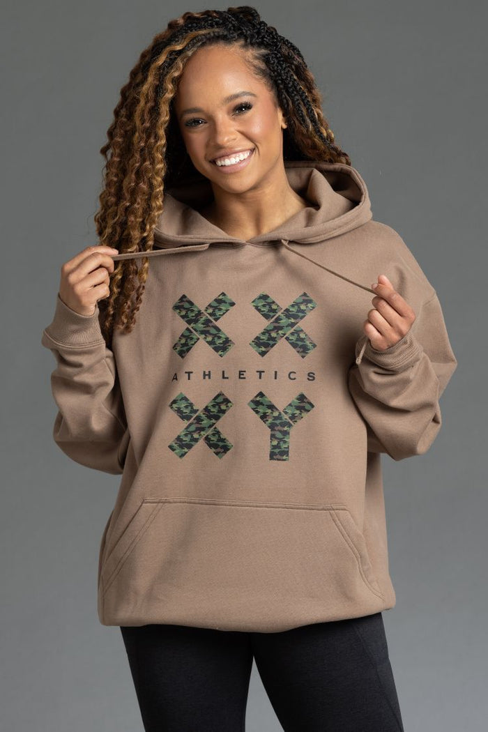 Woman wearing a brown hoodie with 'XY Athletics' logo on a gray background || Mocha