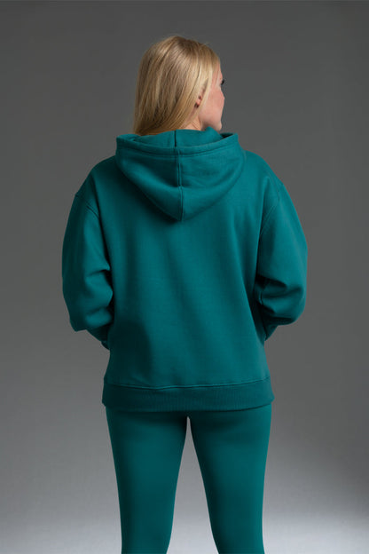 Person wearing a teal hoodie and pants on a gray background || teal