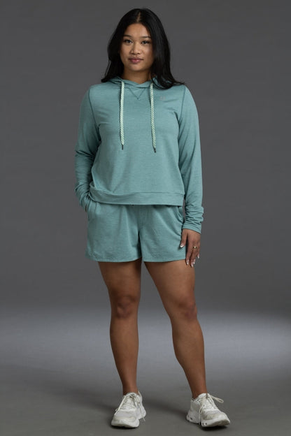Woman wearing a teal hoodie and shorts set on a gray background || Underseas