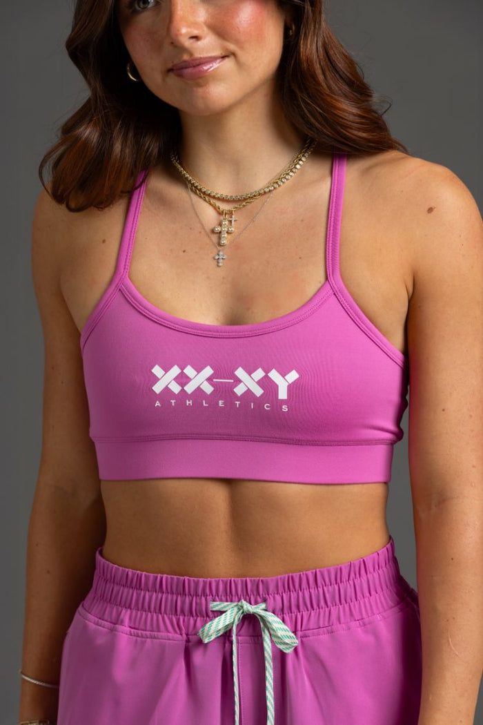 Woman wearing a pink sports bra and shorts with 'XX-XY Athletics' branding. || Bright Fuchsia