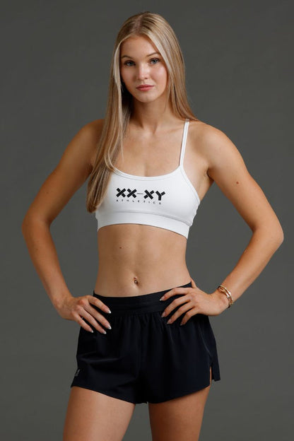 Woman wearing a white sports bra and black shorts with a brand logo || White