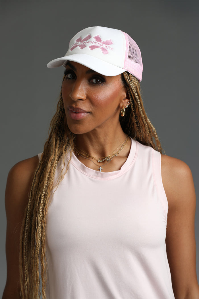 Woman wearing a white cap with pink logo and a light pink sleeveless top against || Pink
